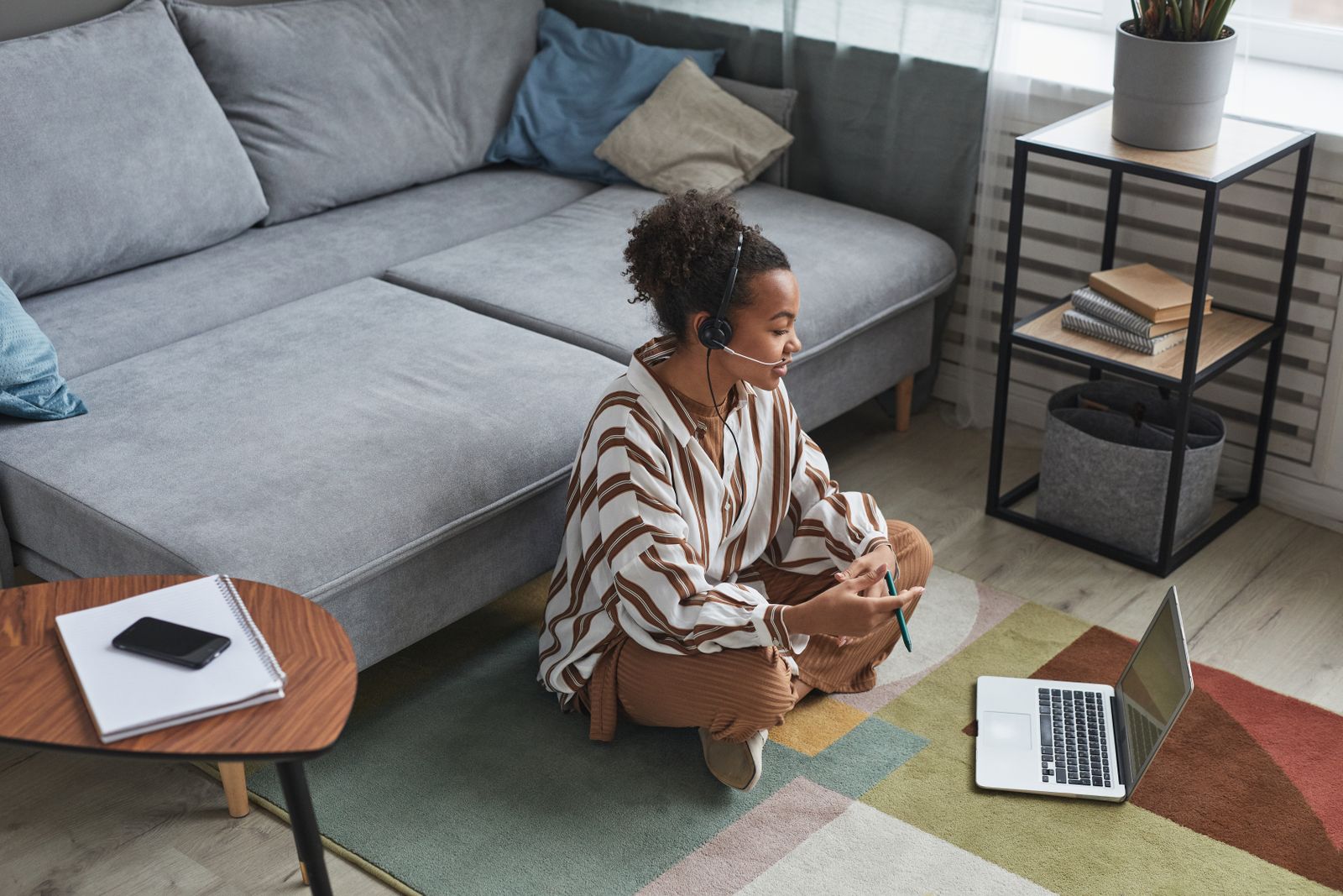 A woman working on a laptop while sitting on the floor at home