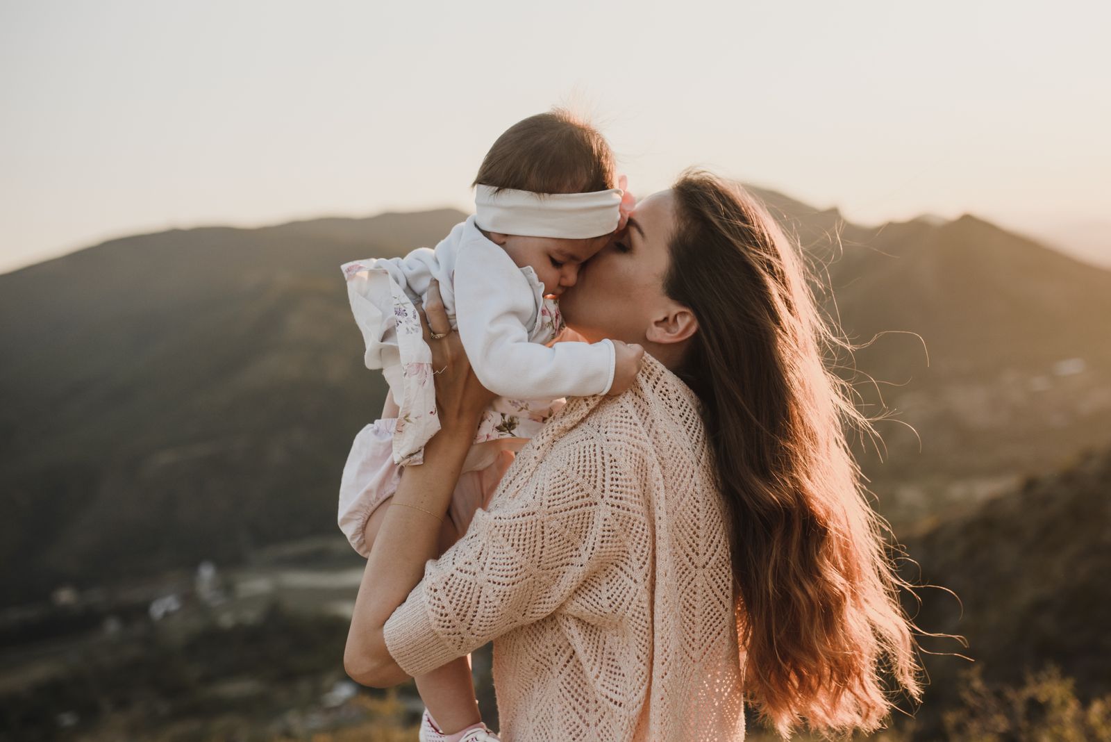 A mother kissing her baby's cheek outdoors