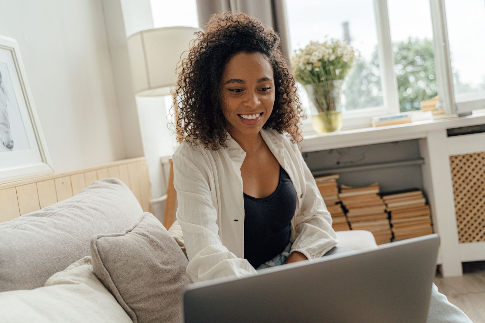 A woman smiling at her laptop on a sofa at home