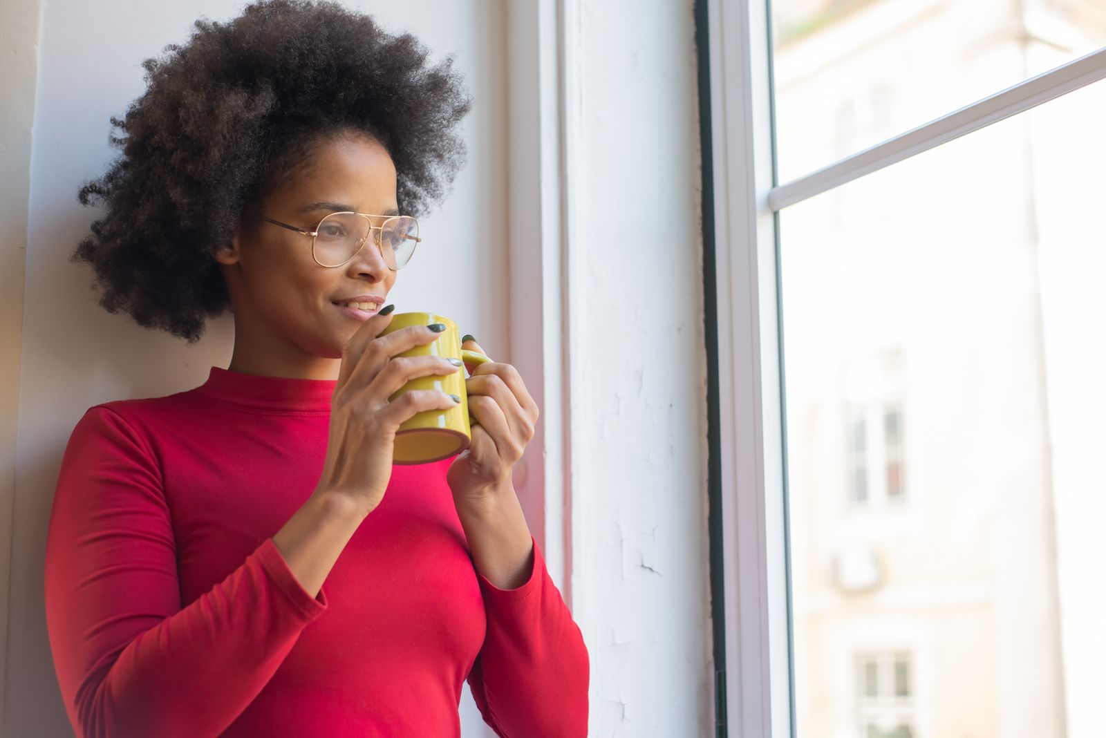 A woman holding a warm mug, looking out a bright window