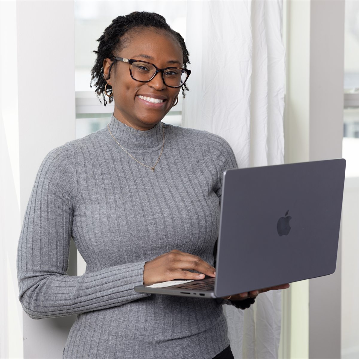 Tiirini Hill, PMHNP-BC, holding a laptop beside a bright window